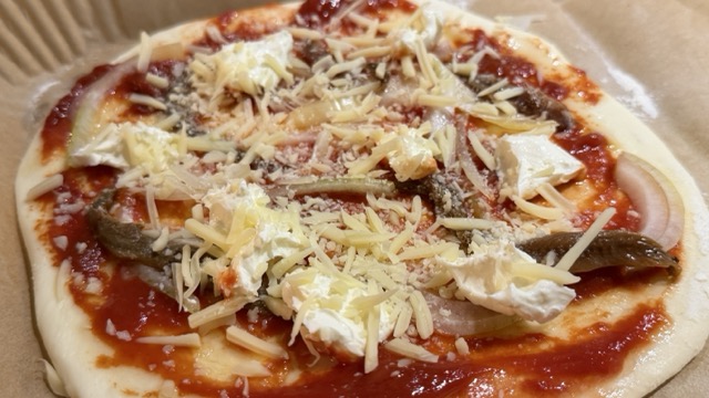 Pizza mit Sardellen, Zwiebeln und Brie belegt, vor dem Backen